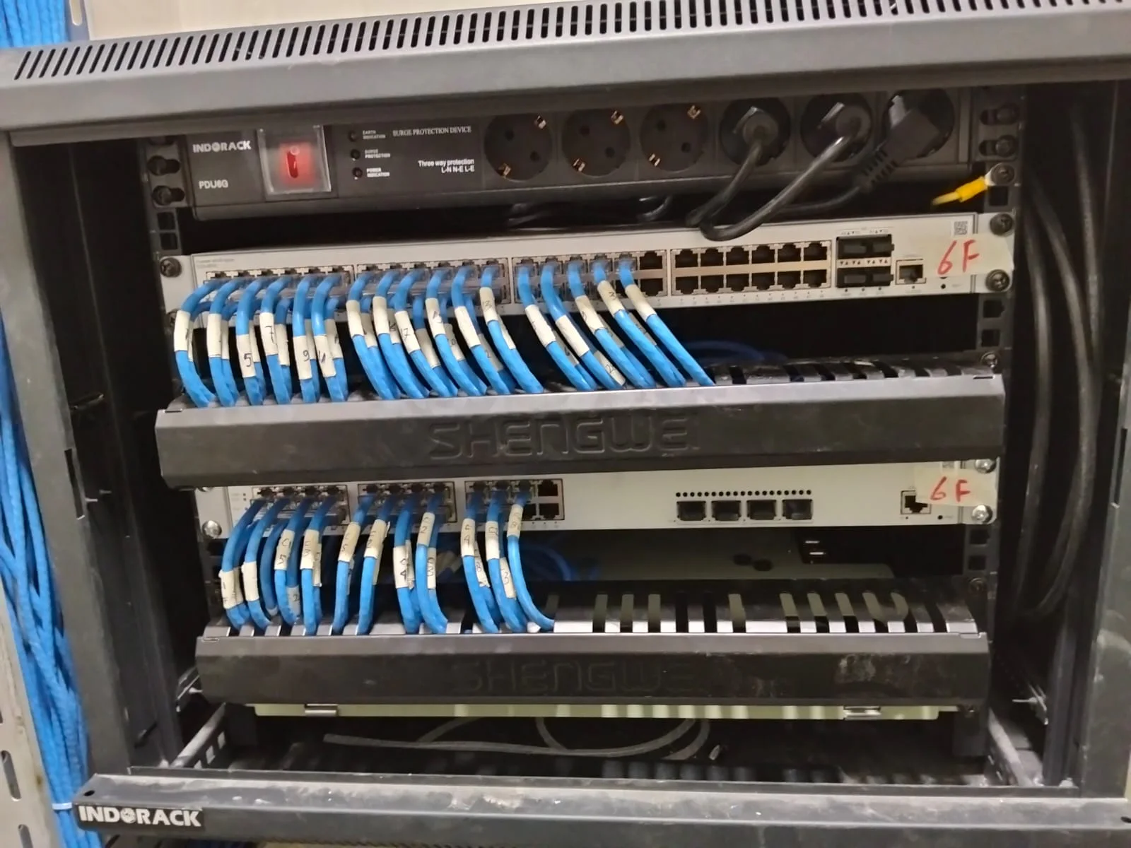 Kabinet jaringan lantai dengan switch 48-port dan kabel patch biru yang diarahkan melalui horizontal cable manager.